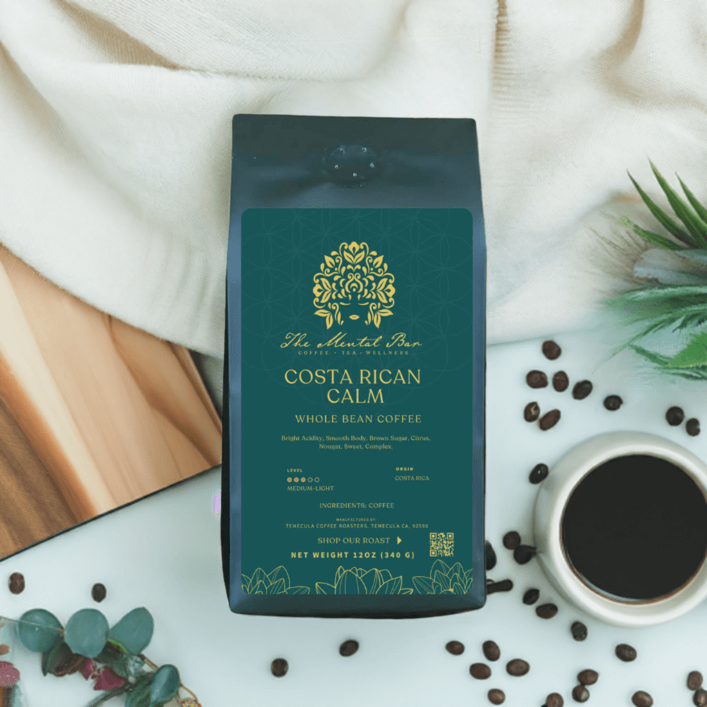 A pack of 'The Mental Bar Costa Rican Calm Whole Bean Coffee' with a green label, brown sugar, citrus, and nougat flavors, and bright acidity. The pack is placed on a white surface with a wooden element, a cup of coffee, and coffee beans around it.