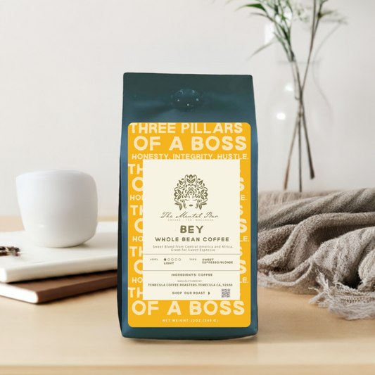 A package of Bey Whole Bean Coffee with the label 'Three Pillars of a Boss' displayed on a table with a white mug and a grey blanket.